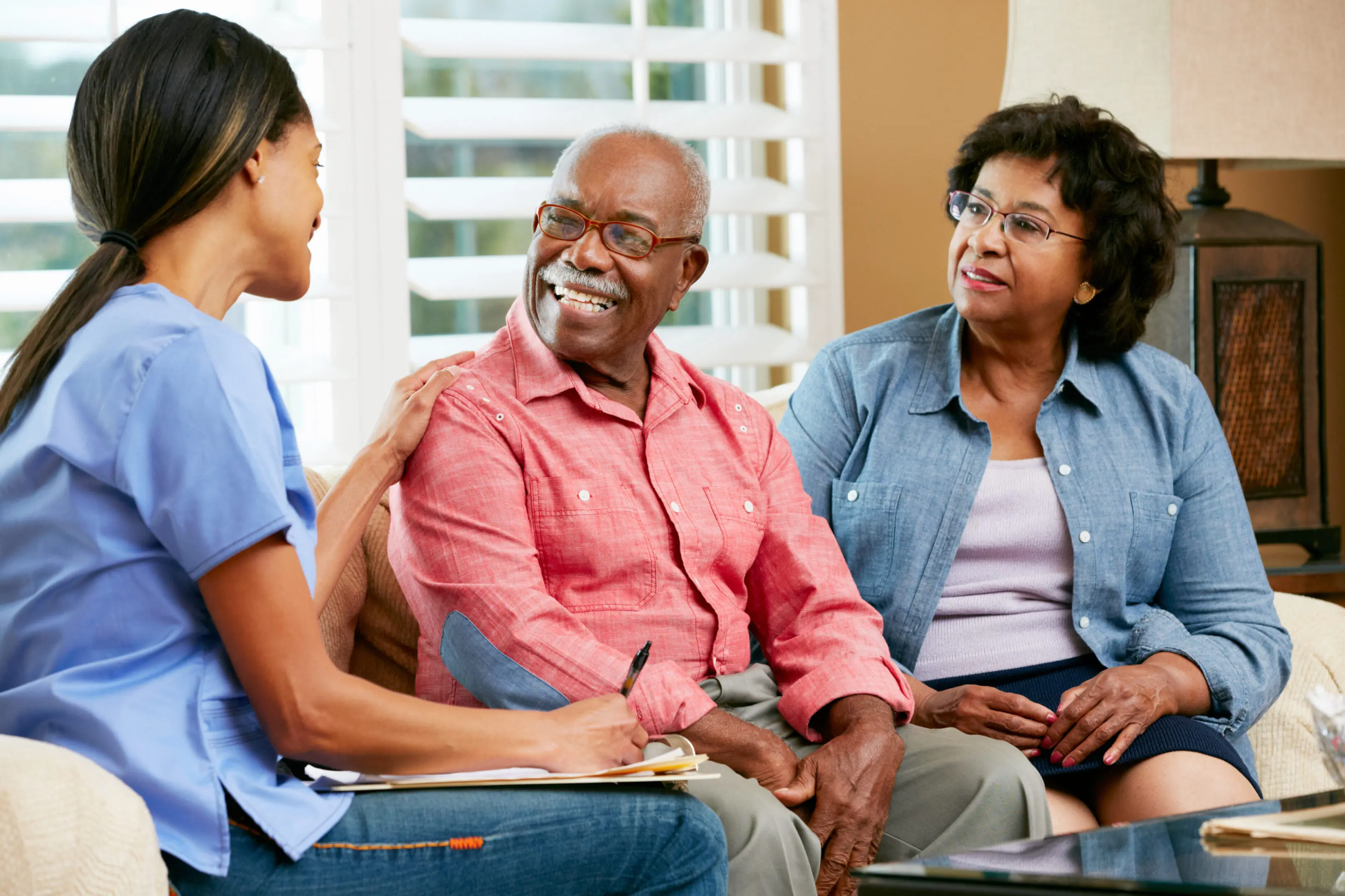 A caregiver attentively talks to an elderly couple in a cozy room.