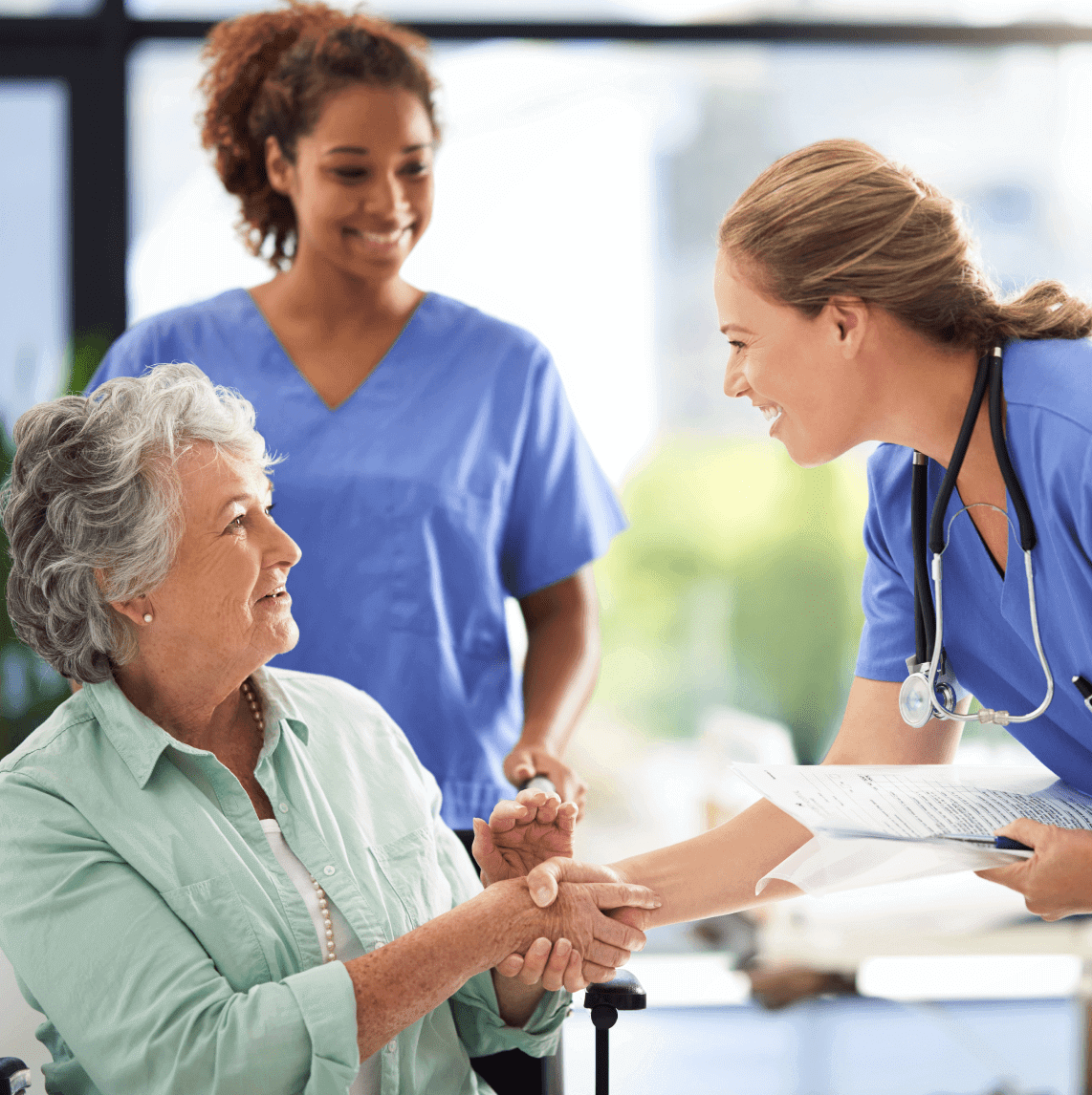 Nurse smiling while assisting an elderly woman in a healthcare setting.