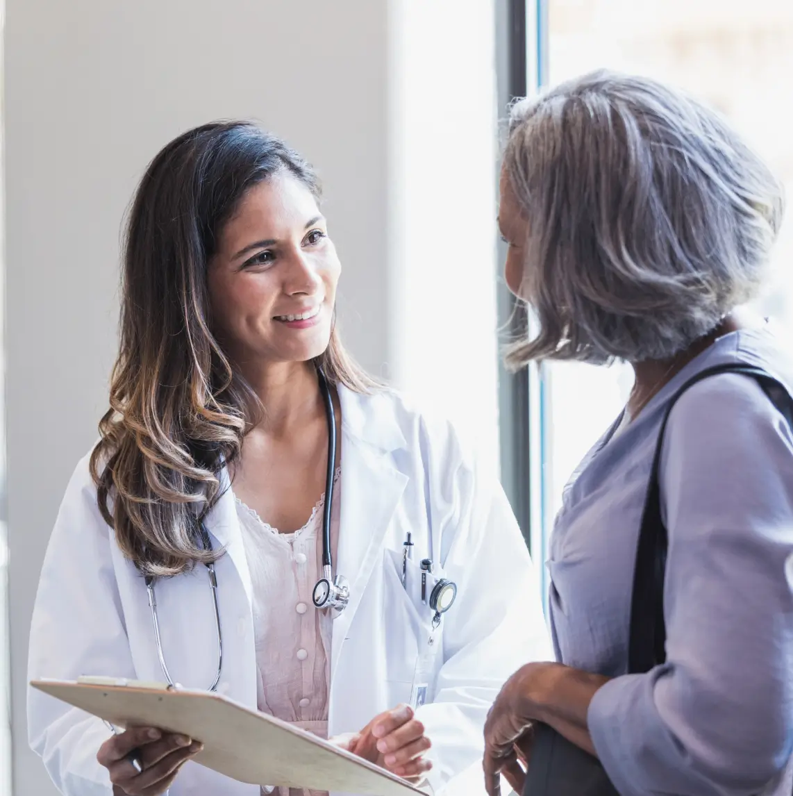 A female doctor consulting with an older female patient in a bright room.
